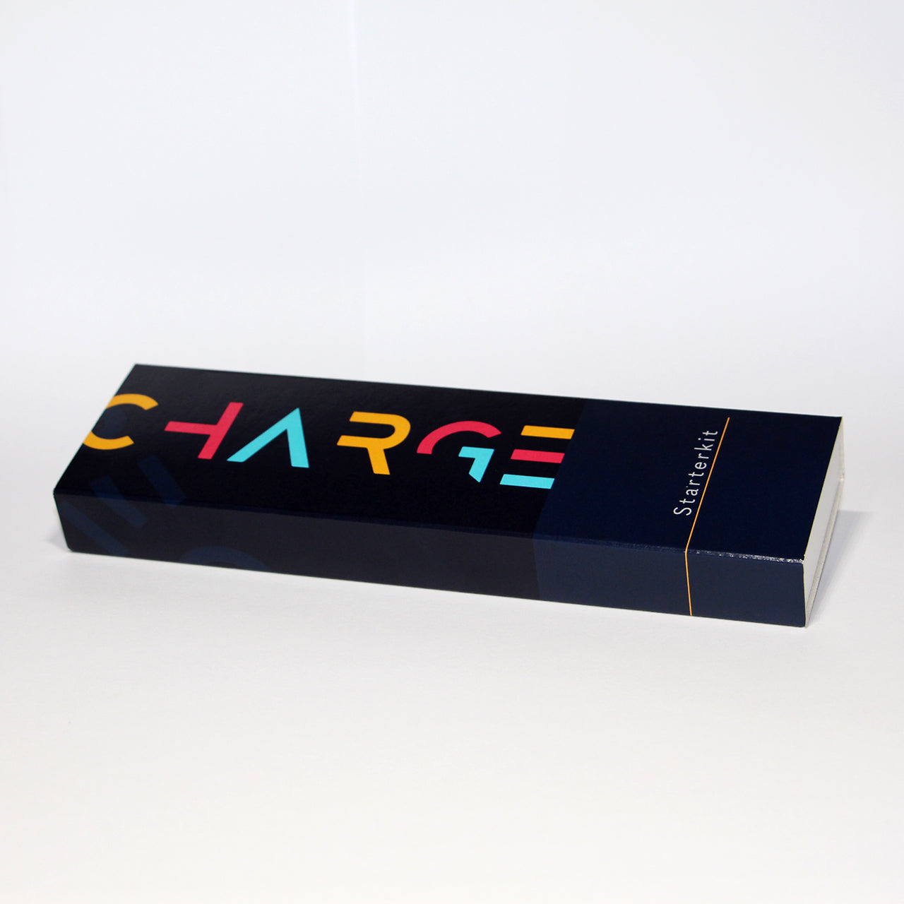 Ein länglicher, dunkelblauer Karton auf dem von links bis zur Mitte in großen gelben, roten und hellblauen Buchstaben "charge" steht. Ganz rechts steht von unten nach oben in weißen Buchstaben "Starterkit".