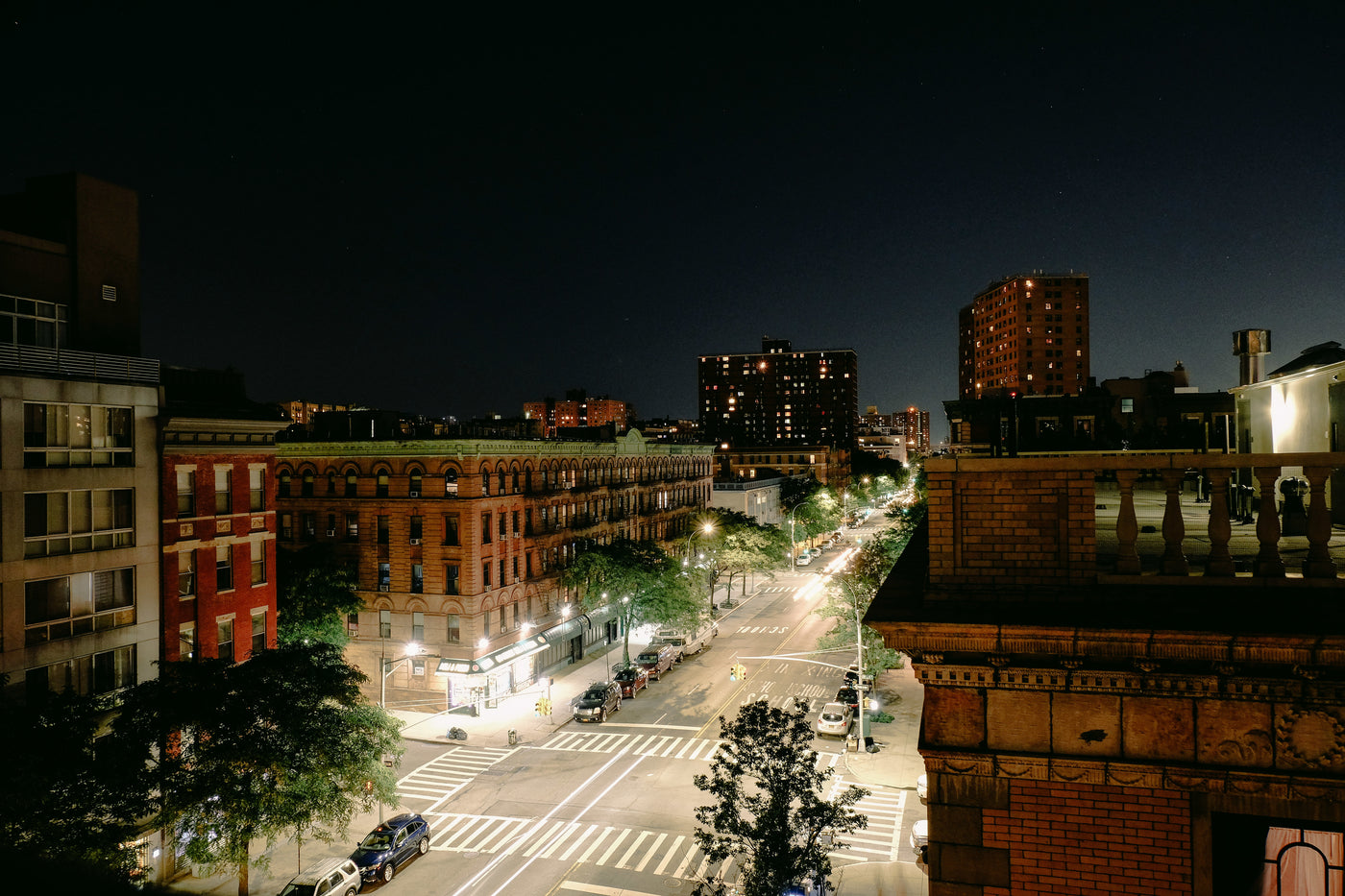 Eine hellerleuchtete Straße bei Nacht. Rechts und links ist sie mit alten, hohen Backsteingebäuden und Bäumen gesäumt.