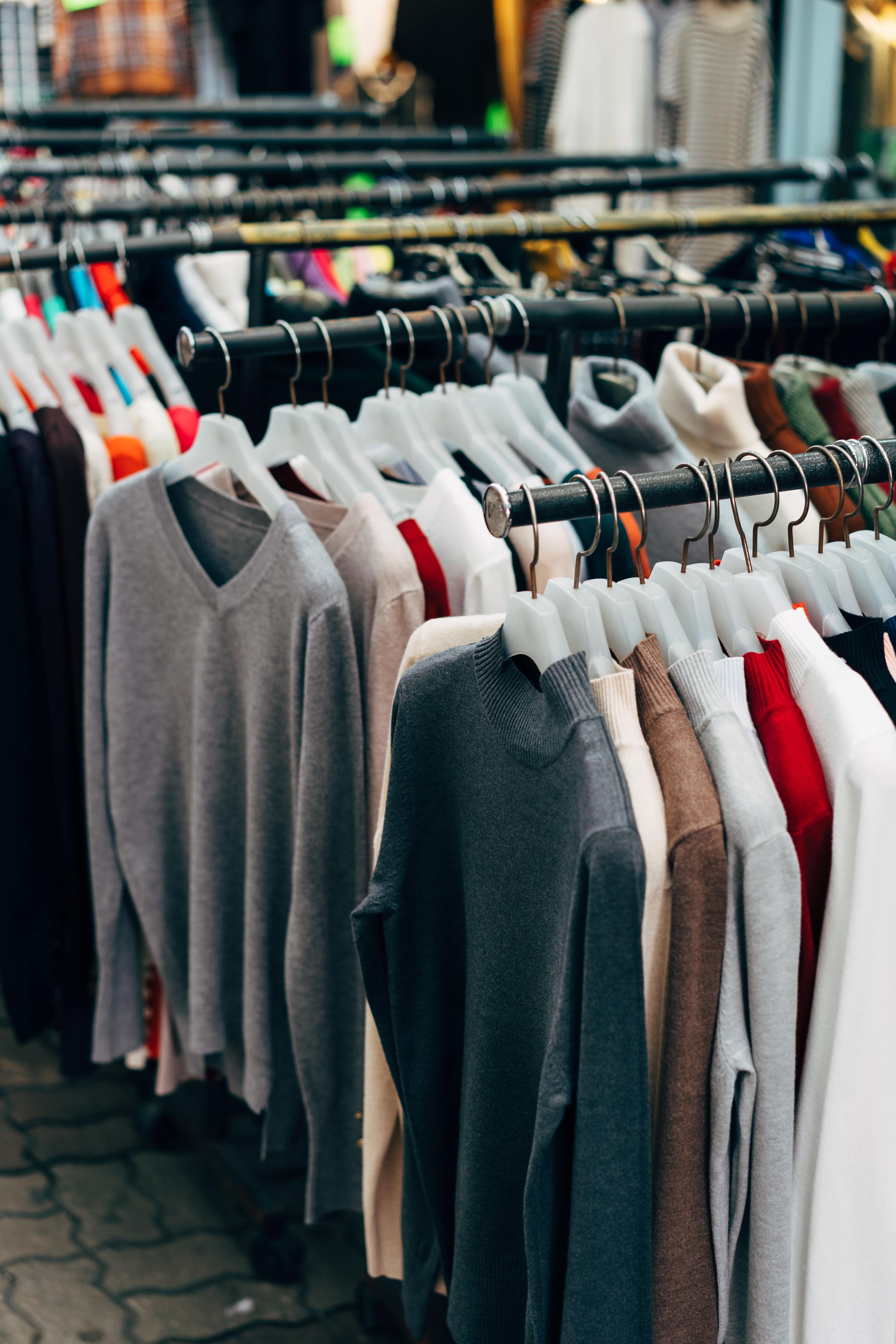 Mehrere Kleiderstangen hintereinander an denen verschiedene Pullover hängen.
