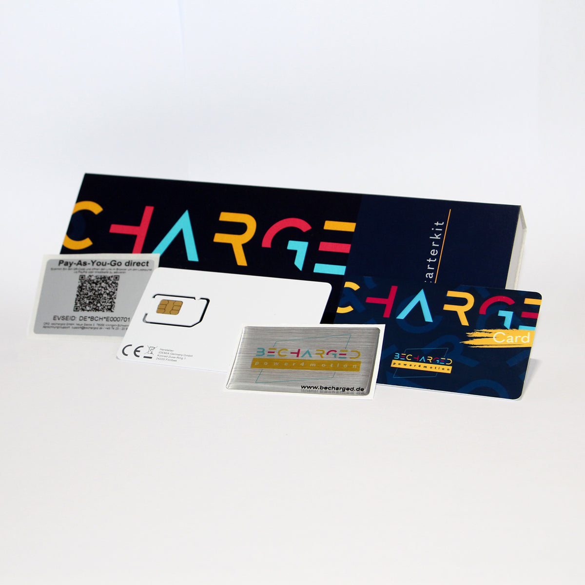 Ein länglicher, dunkelblauer Karton auf dem von links bis zur Mitte in großen gelben, roten und hellblauen Buchstaben "charge" steht. Ganz rechts steht von unten nach oben in weißen Buchstaben "Starterkit". Davor liegt von links nach rechts: ein QR-Code Label, eine SIM-Karte, ein Doming-Aufkleber mit dem becharged Logo und eine RFID-Karte. Die RFID-Karte ist wie der Karton dunkelblau mit dem bunten Schriftzug "charge card".